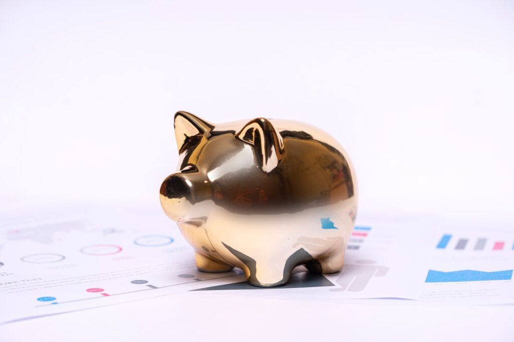 Gold piggy bank resting on financial reports and charts, symbolizing saving money.