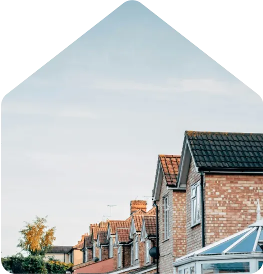 Row of brick terraced houses with pitched roofs and a glass conservatory, under a clear blue sky.